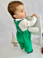 Child wearing green corduroy overalls matched with a white bodysuit with blue piping on the collar.