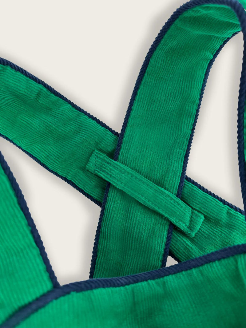 Close up of straps with feeding holder on green children's overalls featuring blue piping. 
