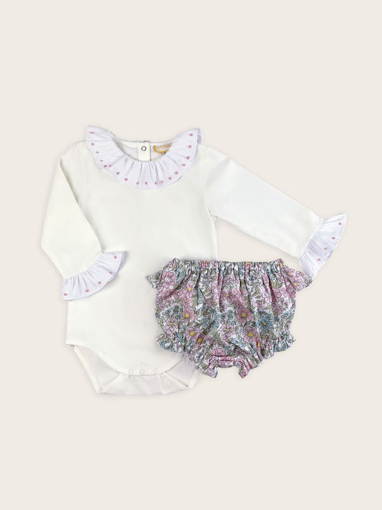 Pink dots embroidered onto the frilled collar and cuffs of a white bodysuit paired with floral bloomers.