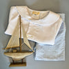 Little Collins Clothing Nautical Boy 2 Piece Set with white double breasted button up shirt and blue and white striped shorts folded up with wooden sailing boat